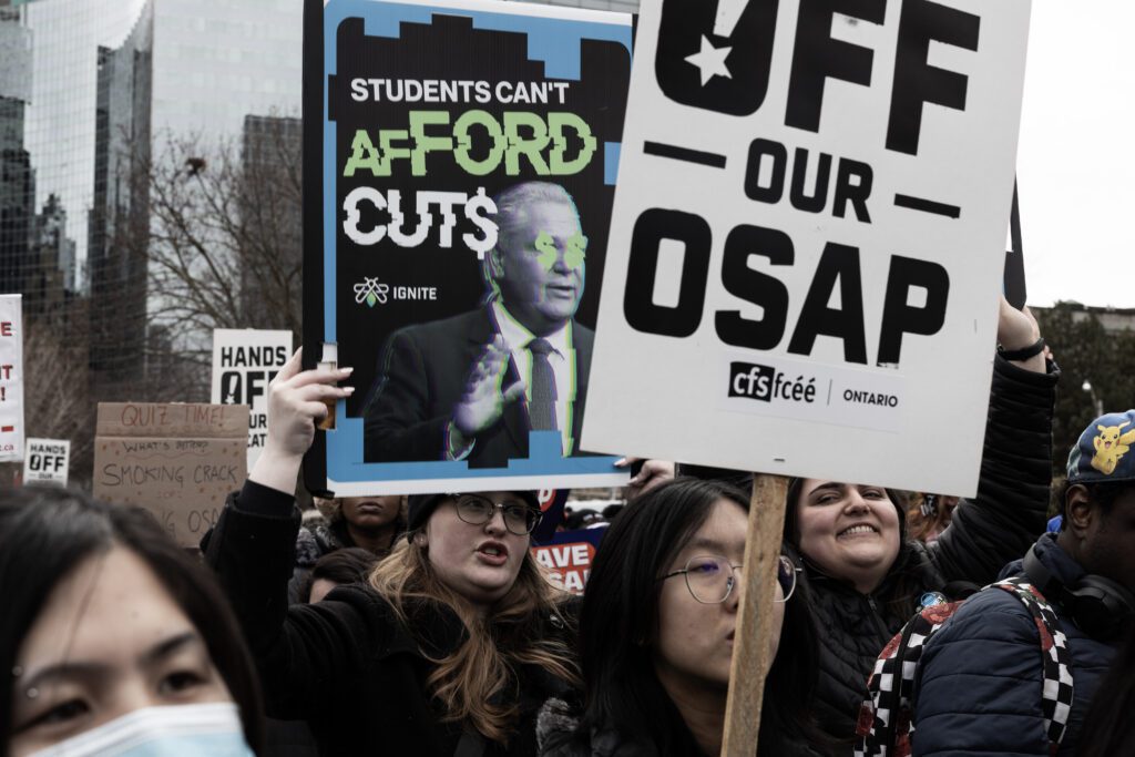 Protesters hold signs against education cuts to OSAP. Signs read, "Students can't afford cuts" and "Hands off our OSAP."