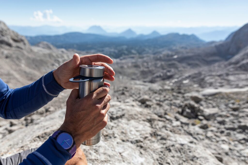 A person is holding a water bottle while hiking in the mountains.