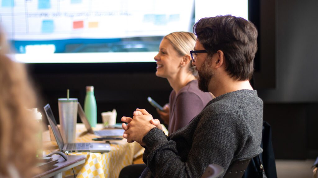 Stephen and Natalie are in a staff meeting. They're laughing at a joke.