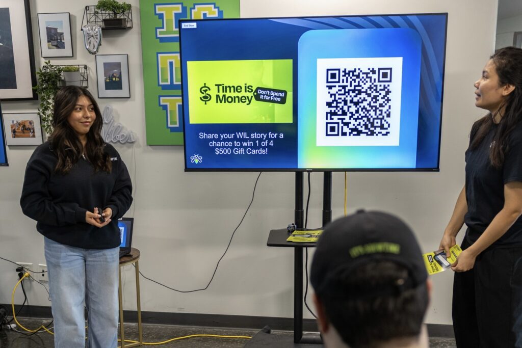 Two IGNITE brand ambassadors are presenting the Time is Money campaign in front of a large monitor; one person sits facing the screen.