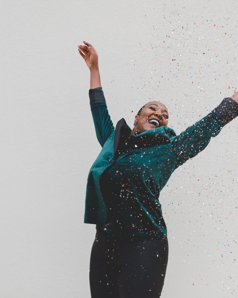 A women smiles with her arms thrown back and is covered in confetti