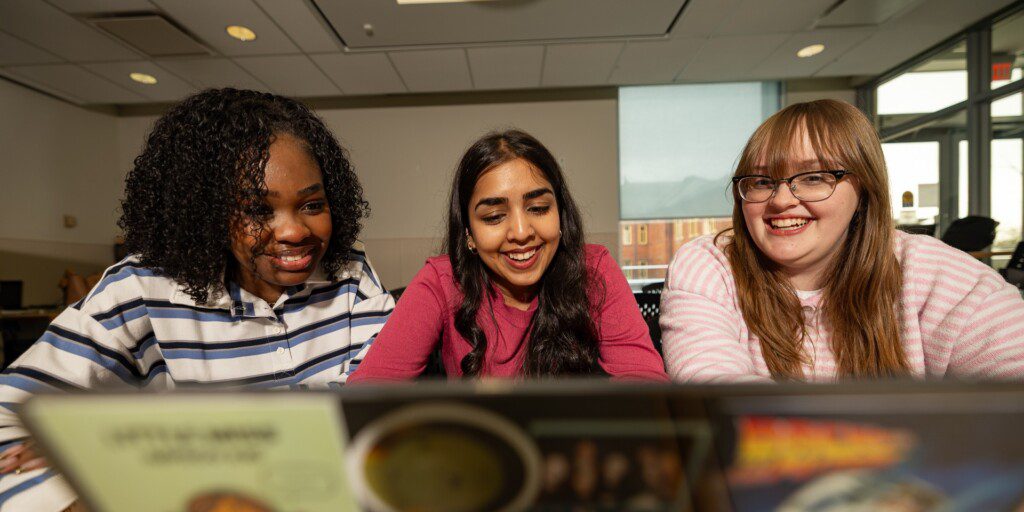 Three students smiling and looking at their laptop