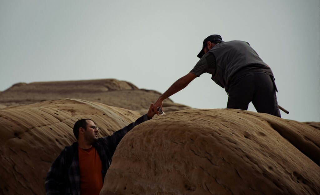 Photo of a man helping another man climb up a cliff