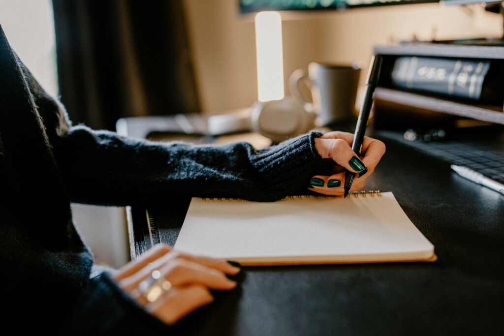 Person writing in a notebook on a dark wooden desk
