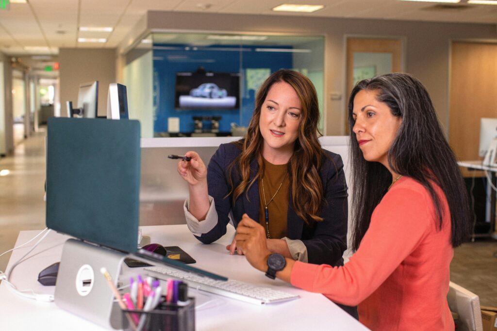 A woman showing another woman applications on a laptop