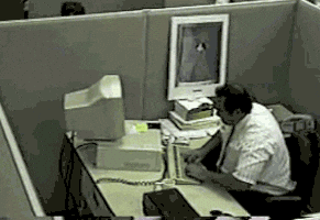 Security camera footage of angry man in an office cubicle smashing his computer with his keyboard. 