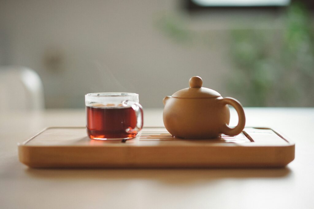 A glass cup with tea near a brown ceramic teapot.