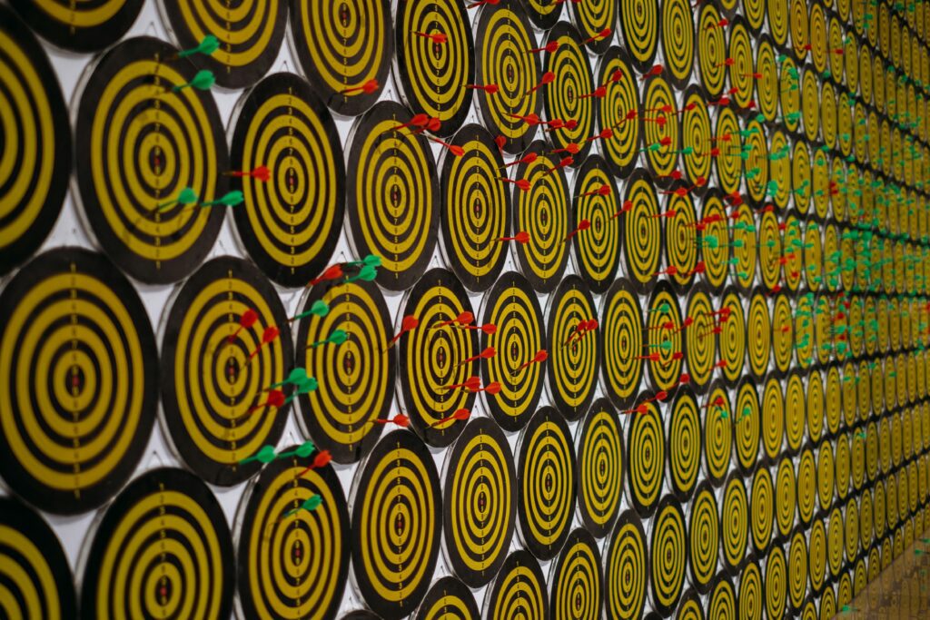 Lots of dart boards on the wall with darts pierced in few of them
