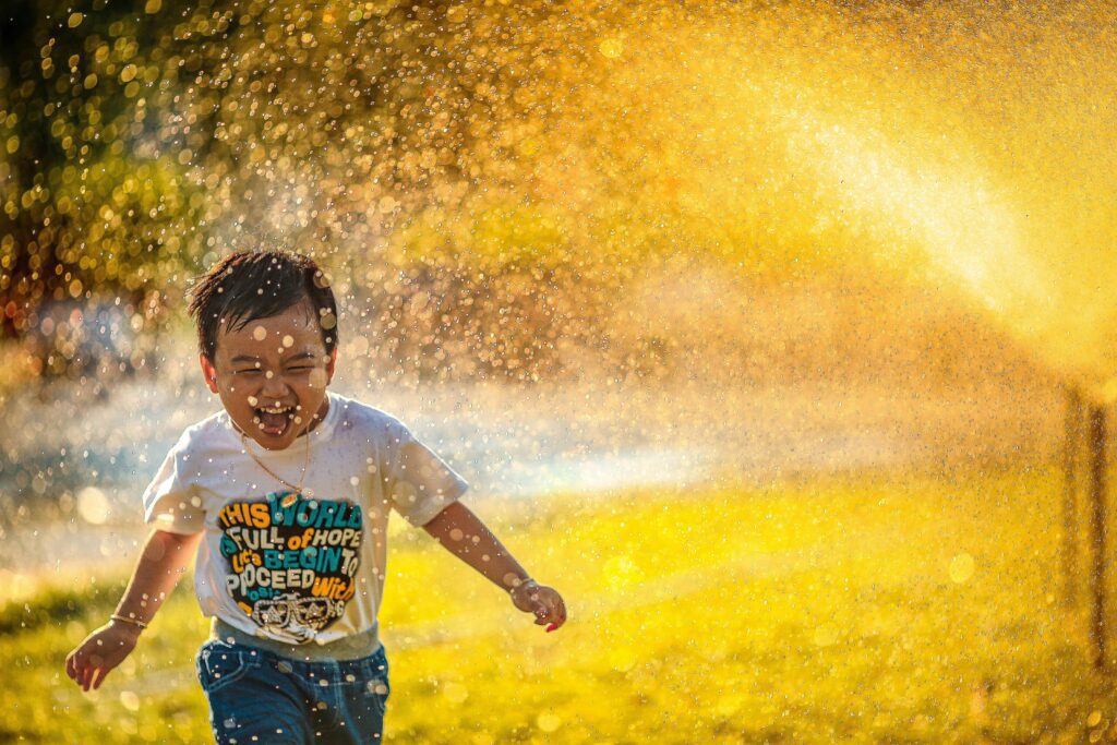 A child running through a garden sprinkler laughing