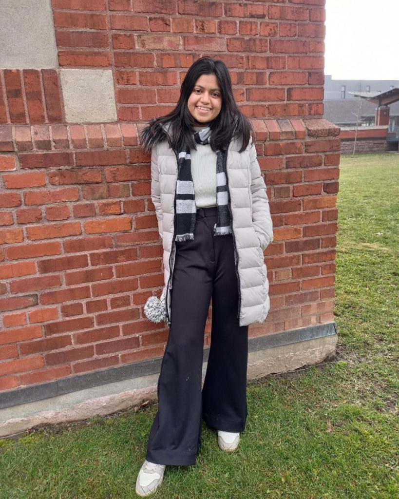 Board of Director Parul Yadav standing and smiling against a brick background.