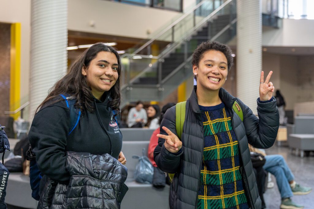 Two students at Humber Polytechnic North campus are smiling and posing with peace signs.