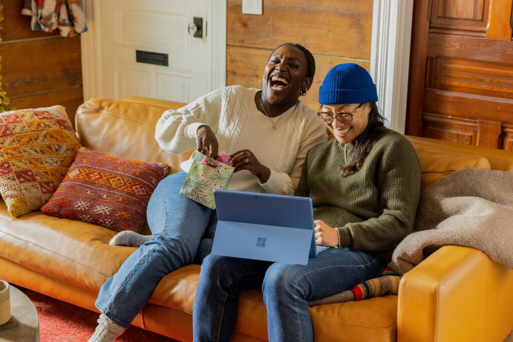 Two people sat on a couch with a laptop, laughing