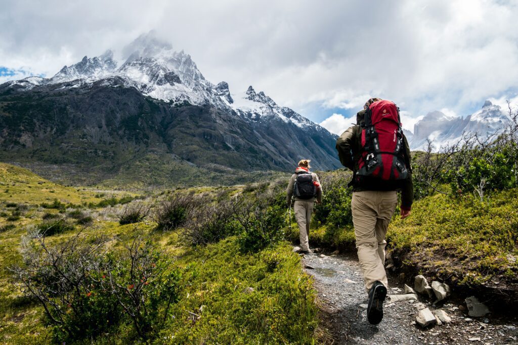 A view of the mountains with two people walking with hike gear