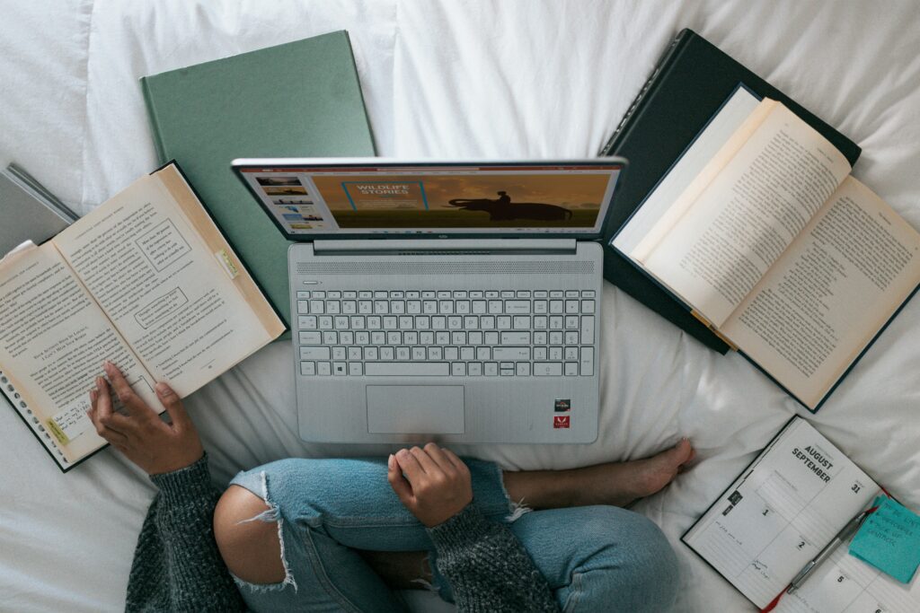 A top view of a woman sat on the bed woth her laptop and books surrounding her