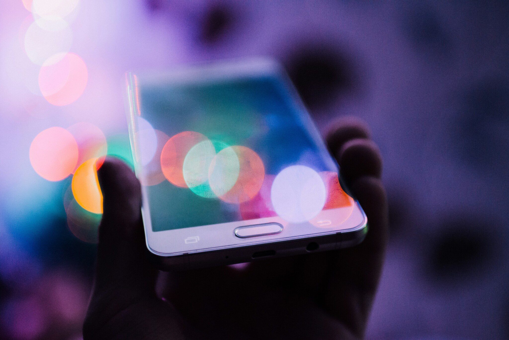 Hand holding a phone over a blurred background with colourful particles sprinkled around