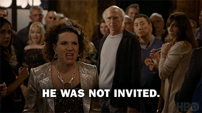 Woman walking through a crowd of adults at a dinner party in dim lighting yelling "he was not invited", as the same words are present in white lettering at the bottom of the image.