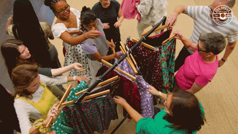 Bunch of people grabbing clothes from a singular clothing rack