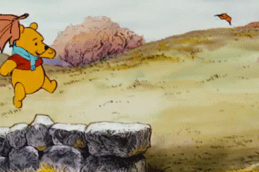 Yellow cartoon bear from Winnie the Pooh skipping along a stone wall, and tumbles off to the grass while trying to catch a leaf flying through the air.