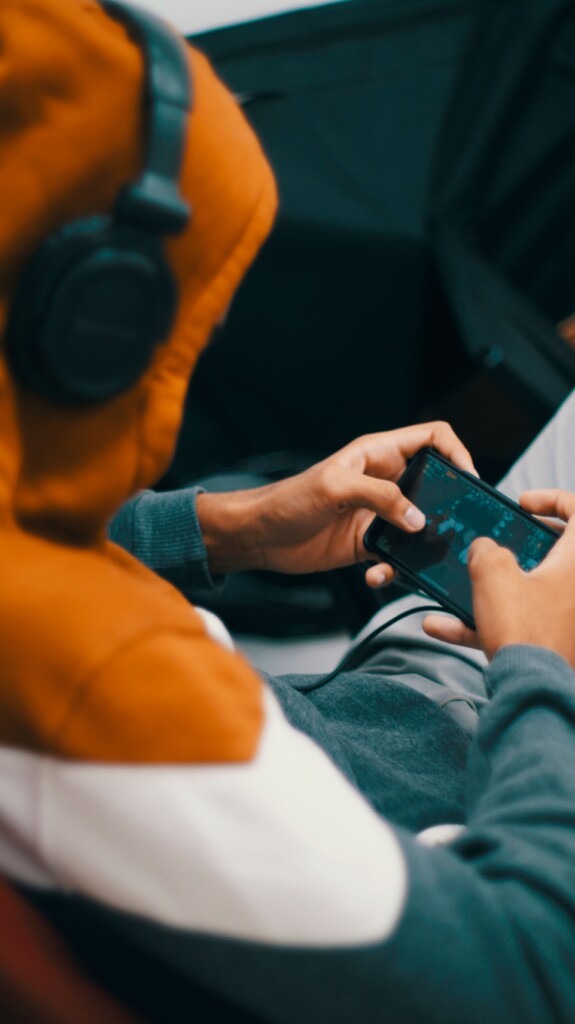 Person in orange hoodie wearing headphones playing a game on their phone. 