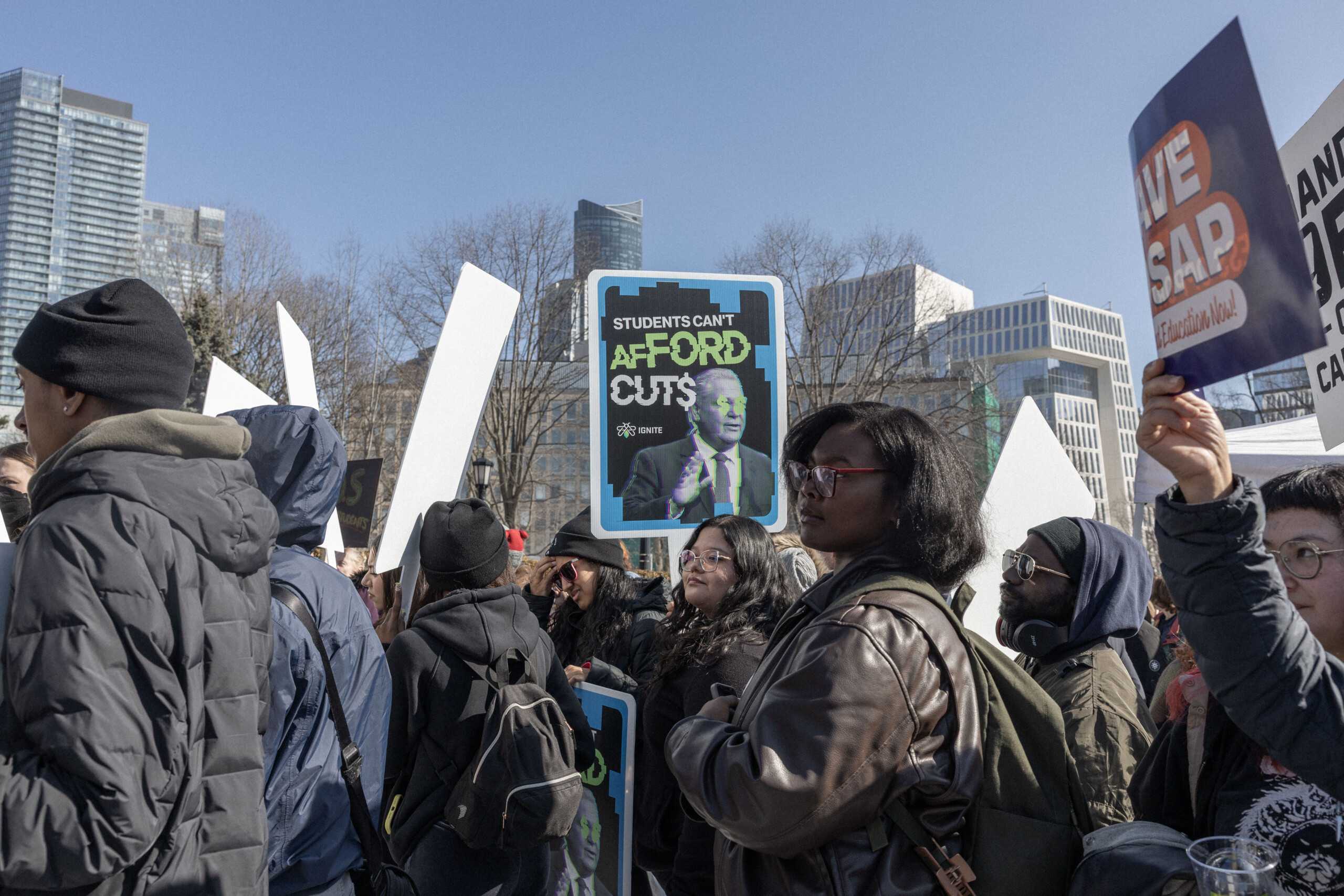 Students protesting OSAP budget cuts outside Queens Park, holding signs.